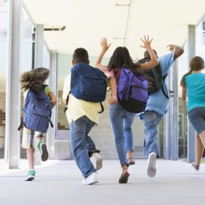 Rear view of elementary school pupils running outside